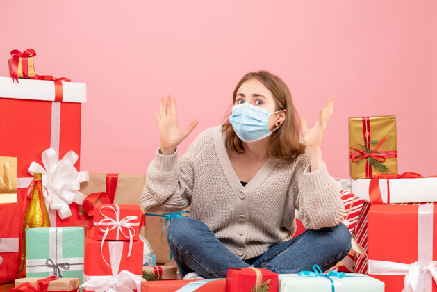 礼物正面图：坐在圣诞节周围的年轻女性戴着无菌面具出现人面具成人