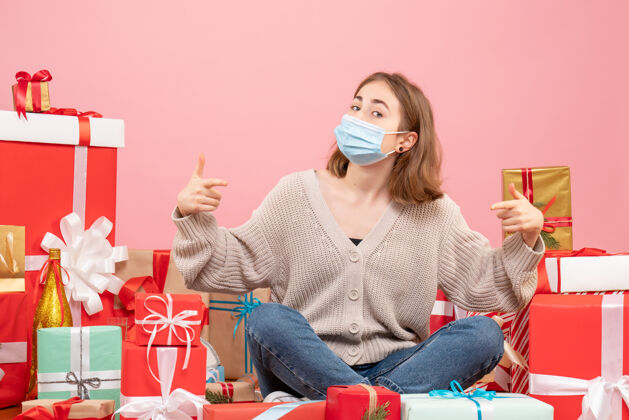 消毒正面图：坐在圣诞节周围的年轻女性戴着无菌面具出现微笑圣诞节年轻女性