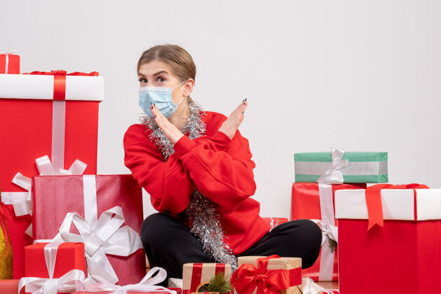 生活正面图：年轻女性戴着无菌面具坐着 手里拿着圣诞礼物面具坐着病毒
