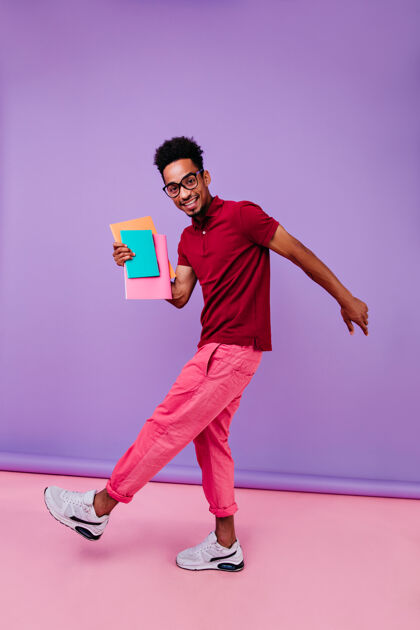 时尚快乐的国际学生考试后跳舞的全长肖像穿着粉红色裤子的聪明的非洲男人拿着书站着男孩非洲裔美国人种族