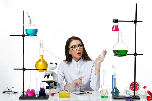正面前视图穿着白色医疗服的女化学家坐在白色背景上实验室病毒冠状病毒大流行科学化学品视图坐着