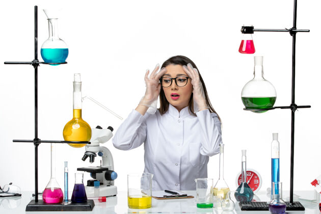 坐着前视图穿着白色医疗服的女化学家坐在白色背景上解决方案科学大流行病毒covid实验室前面工作大流行