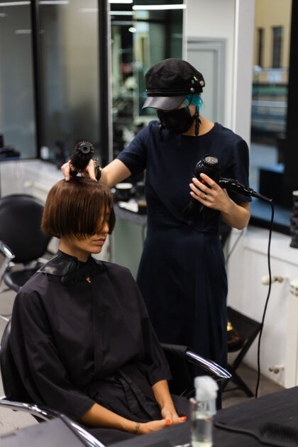 设备一个专业的女理发师给客户理发这个女孩戴着面具坐在美容院里脸人时尚