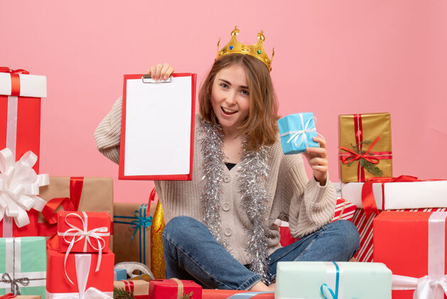 年轻的女性正面图年轻女性围坐在礼物旁边 手里拿着纸条圣诞节房子粉红色