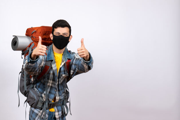 背包正面图：背着背包和面具的快乐男性旅行者竖起大拇指摄影师娱乐拇指