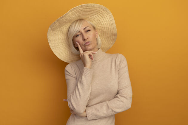 自信自信的金发斯拉夫女人 戴着沙滩帽 手放在橙色的下巴上女人手成人