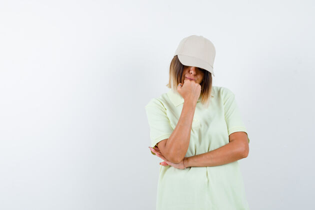 站年轻女士穿着t恤 戴着帽子 站在思考的姿势 看着深思熟虑的前景色女孩微笑自然