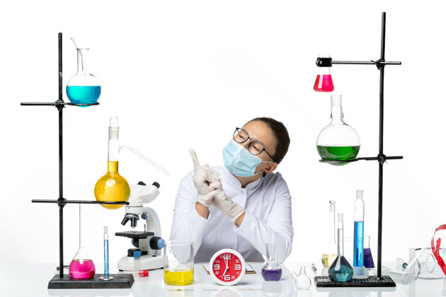 化学家前视图：穿着白色医疗服的女化学家戴着面罩坐在白色办公桌上 解决方案化学家病毒冠状病毒-飞溅实验室前面病毒实验室