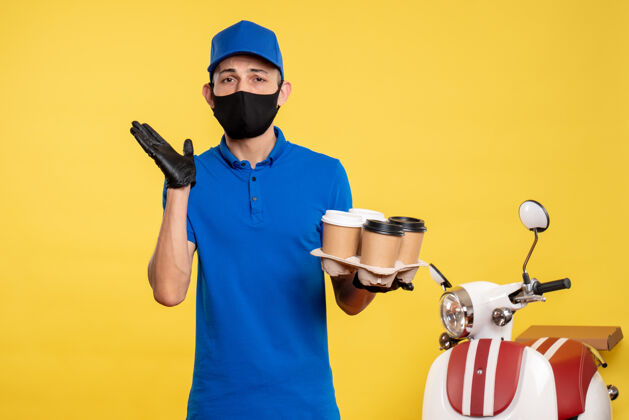 人正面图戴着黑色面具的男信使拿着咖啡在黄色工作服上工作大流行制服人