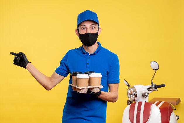 人正面图：身穿蓝色制服 戴着面具的男信使拿着咖啡 穿着黄色制服 工作服 工作服男性信使人正面