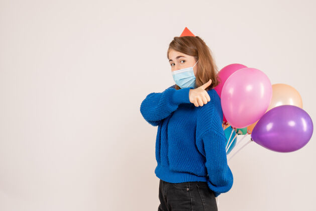 人正面图：戴着无菌口罩的年轻女性把五颜六色的气球藏在背后圣诞节面具消毒