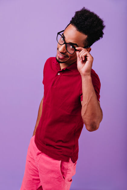 乐观穿着红色t恤的英俊的年轻人开玩笑地摆姿势乐观的非洲男孩摸他的眼镜紫色现代模特