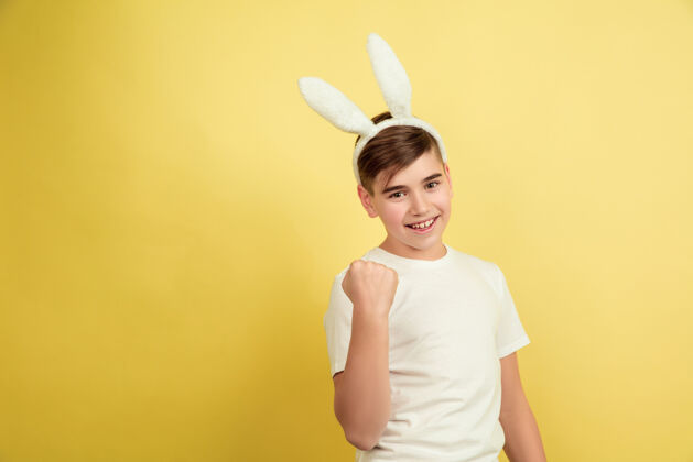 肖像白人男孩作为一个复活节兔子在黄色的工作室背景复活节快乐的问候惊喜表情问候