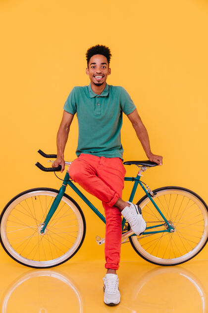快乐穿着红色裤子的无忧无虑的骑自行车者的全长肖像活跃的非洲男子与自行车一起享受的室内照片时尚表情模特