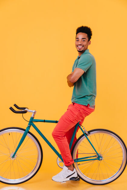 活跃自信的黑人坐在自行车上双臂交叉的全长照片令人高兴的非洲男人放松的肖像模特自行车着装