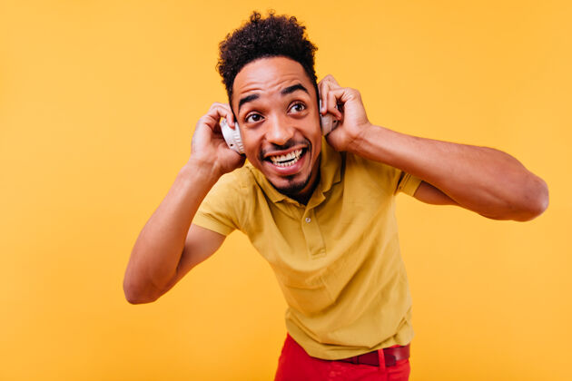 乐趣大黑眼睛的帅哥在听音乐戴着白色耳机的快乐非洲男模的室内照片年轻人年轻自信