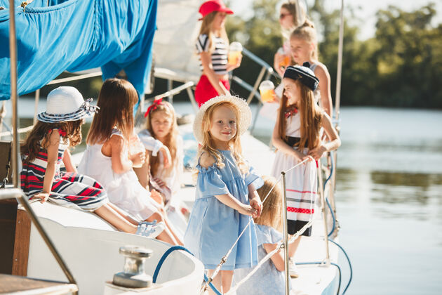 船孩子们在游艇上喝着橙汁十几岁或十几岁的女孩在户外蓝天下女孩河流阳光
