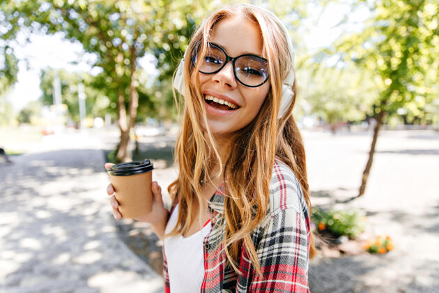 散步在公园里喝茶的笑容可掬的女人在大自然里喝咖啡的时髦白人女孩人周末寒冷