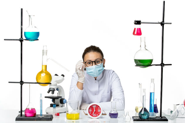 面具前视图穿着医疗服的女化学家带着面罩坐在白色背景上的溶液飞溅病毒化学科维德实验室专业医学前面