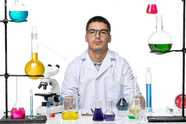 前面正面图：身着医疗服的男性化学家坐在白色背景上 用不同的溶液进行病毒实验室化学测试查看药剂师化学