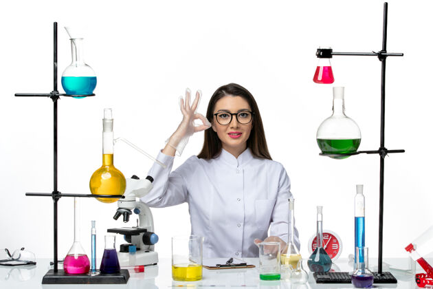 病毒前视图穿着白色医疗服的女化学家正坐在白色背景的解决方案上科学冠状病毒大流行实验室病毒药品医生成人