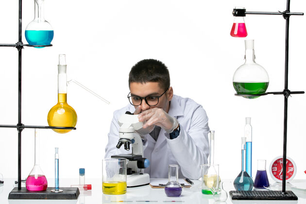 视图前视图：穿着白色医疗服的男性化学家在白色背景上使用显微镜病毒实验室冠状病毒-疾病科学医学使用烧杯
