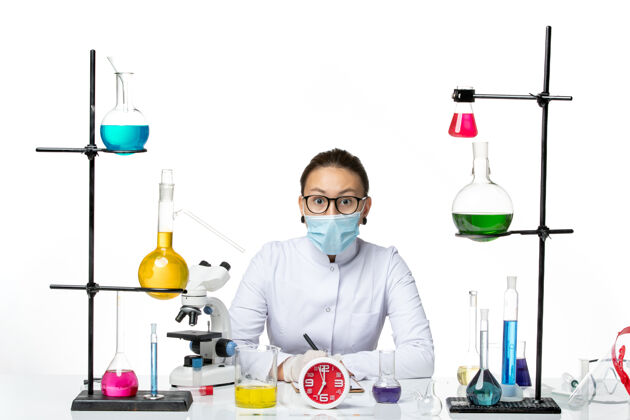化学前视图穿着白色医疗服的女化学家带着面具在浅白色背景上写笔记化学家病毒covid-飞溅实验室笔记实验室面具