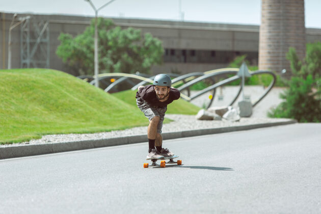 男孩在阳光明媚的日子里 在城市街道上玩滑板的人穿着装备的年轻人在沥青路面上骑行和玩长板休闲活动 运动 极限 爱好和运动的概念游戏平衡年轻