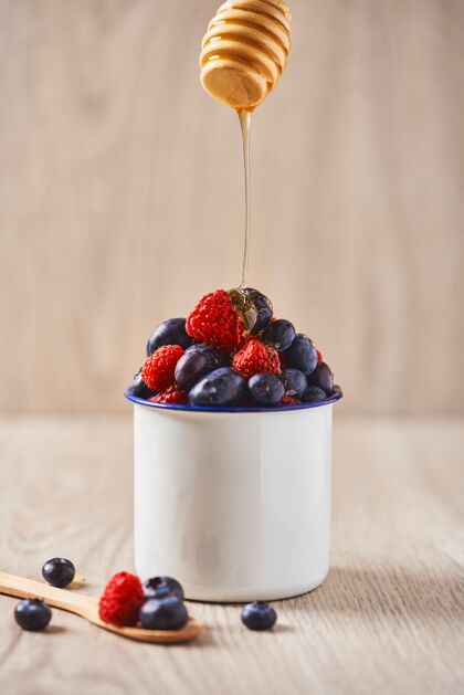 圆形一个白色的碗里装满了蓝莓和草莓 上面滴着蜂蜜食物勺子花园
