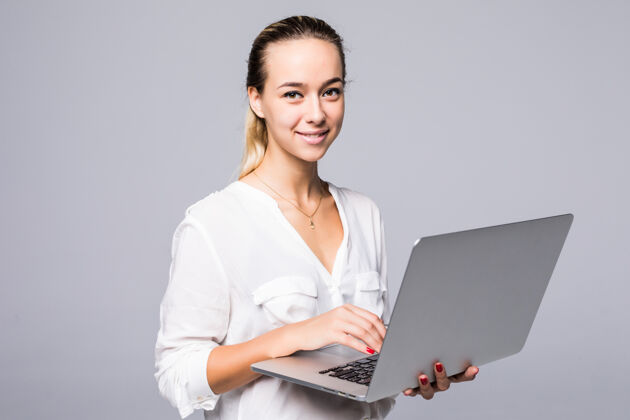金发侧视图一个快乐的年轻女子在笔记本电脑上打字的肖像隔离在灰色的墙上微笑电脑笔记本电脑