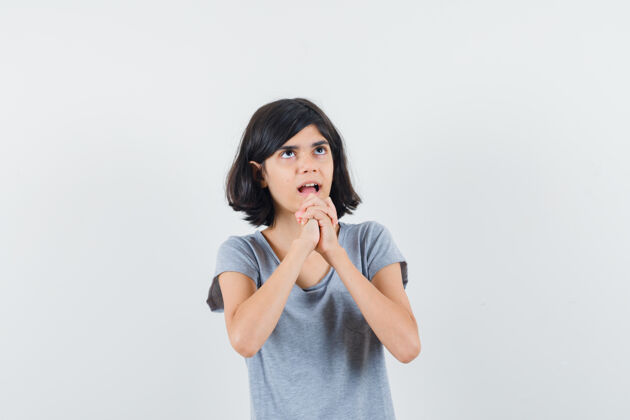 肖像小女孩抱着祈祷的手势在t恤衫和期待的手 正面视图欢乐扣手势