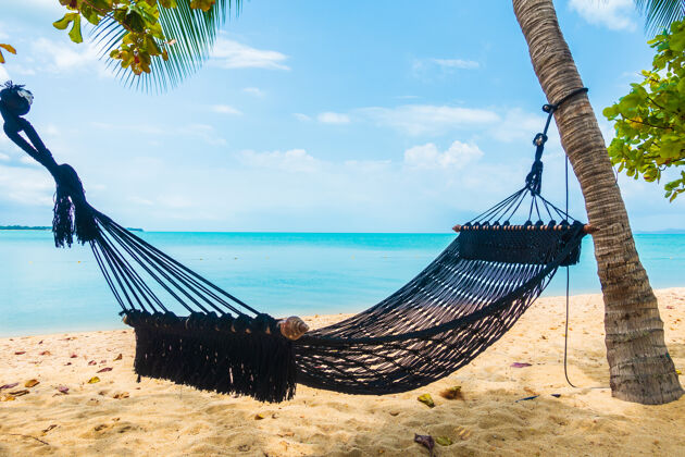 田园诗空空的吊床荡在沙滩 大海 白云和蓝天之间 供旅游度假之用地平线伞休息