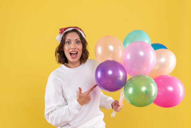 快乐正面图美丽的女性手持彩色气球站在黄色的年乐趣多彩