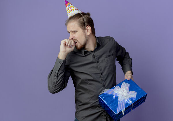 盒子戴着生日帽的焦急帅哥拿着礼盒望着紫色墙上孤立的一面礼物壁板男人