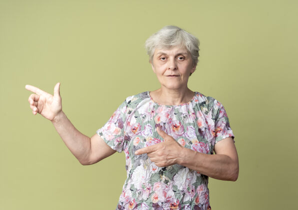 手自信的老妇人在一旁指指点点 两只手分别放在橄榄绿的墙上橄榄女人点