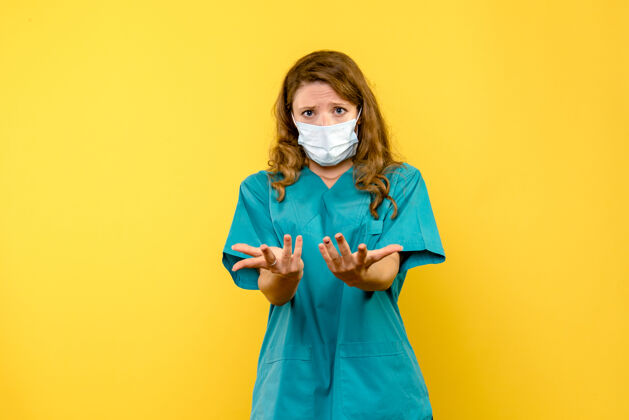 流行病黄墙上戴着面具的女医生的正视图成人人医生