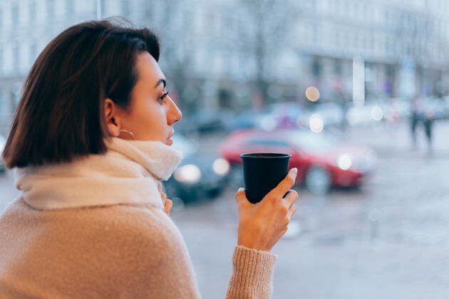 年轻一个女孩在舒适的咖啡馆里用一杯热咖啡取暖窗户杯子成人