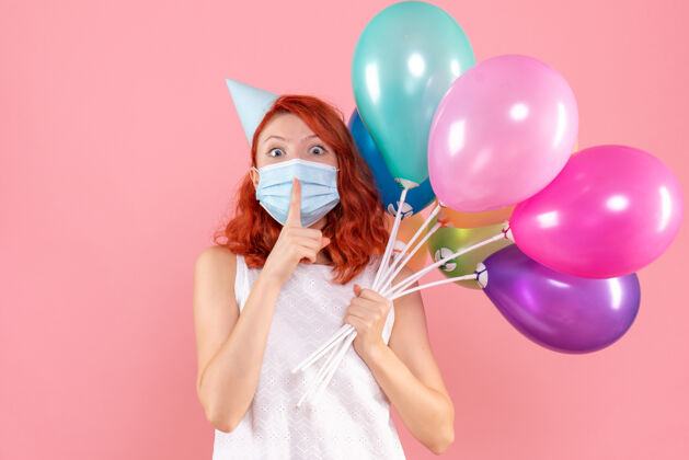 年轻女性正面图年轻女性手持彩色气球在粉红色的面具上病毒颜色庆祝
