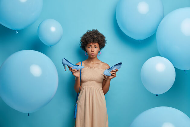 选择心烦意乱的女人穿高跟鞋时长了老茧 穿着鸡尾酒会礼服 心情不好 聚会后很累 孤立在蓝色的墙上装饰着充气气球女人衣服收藏魅力肖像穿着