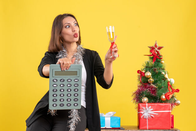 举行圣诞节的心情与惊喜美丽的女士站在办公室里 拿着计算器在黄色的办公室里举酒肖像圣诞节提高