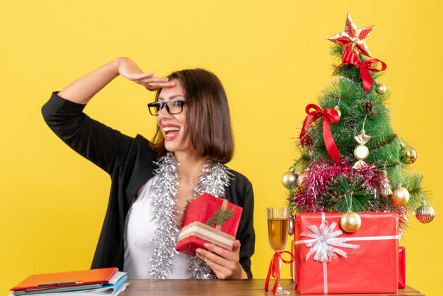 眼镜一位穿着西装 戴着眼镜的商务女士拿着礼物 坐在一张桌子旁 桌子上放着一棵圣诞树人人桌子