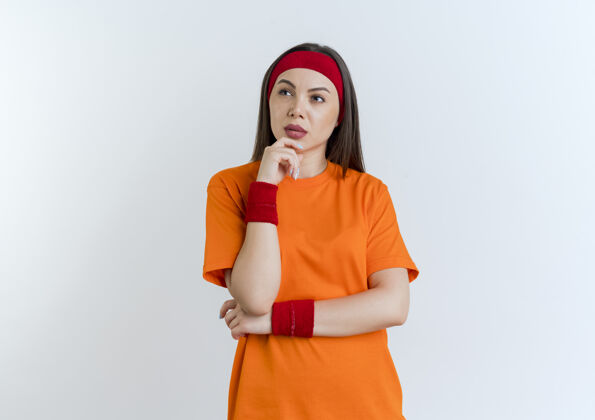 腕带体贴的年轻运动女性戴着头带和腕带抚摸着下巴看着身边孤立头带下巴触摸
