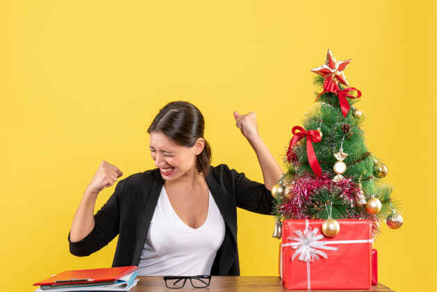 老师在黄色的办公室里 一位穿着西装的年轻女士在装饰好的圣诞树旁 心满意足肖像圣诞支持