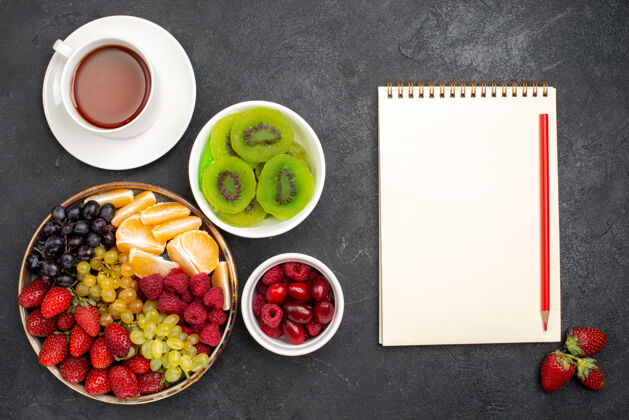 桌子顶视图水果成分草莓葡萄覆盆子和橘子茶在深灰色的桌子上杯子膳食热带