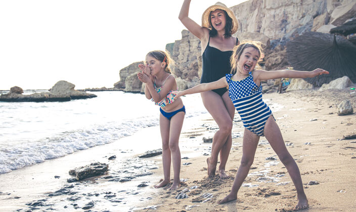 散步一位年轻的母亲和两个小女儿在海边玩得很开心 一边跳舞 一边笑一家人度假愉快跳舞阳光假期