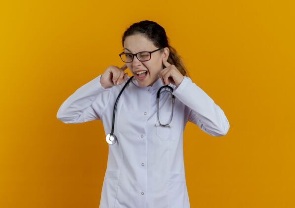 年轻年轻的女医生穿着医用长袍戴着听诊器戴着眼镜闭着耳朵隔离耳朵眼镜女士