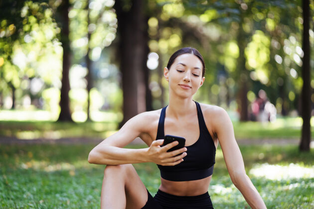 运动拥有智能手机自然背景的健身女孩 喜欢运动训练在户外使用手机的女人休息休息跑步