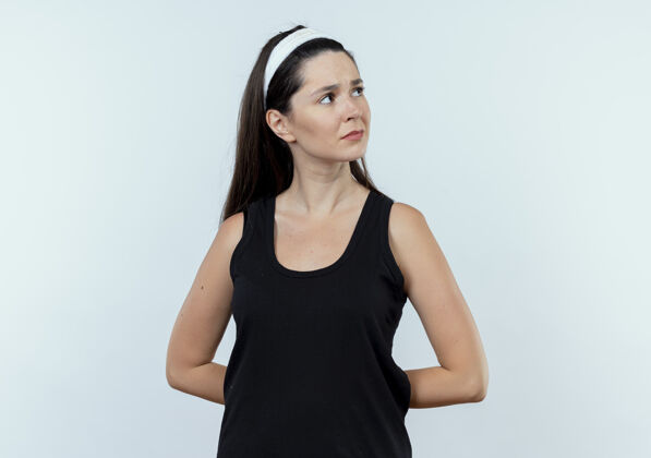 年轻戴着头巾的年轻健身女士站在白色的背景上 脸上带着沉思的表情望向一边沉思健身面子