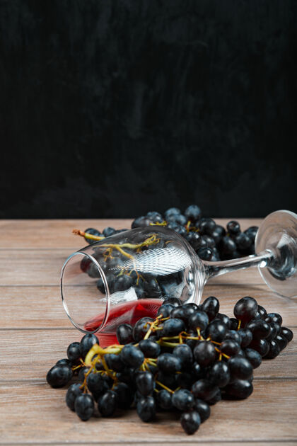 前视图一束黑葡萄和一杯葡萄酒在黑暗的背景下高品质的照片桌子玻璃自然