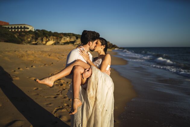 海岸线一对美丽的夫妇在他们的婚礼上互相亲吻的照片白色阳光海洋